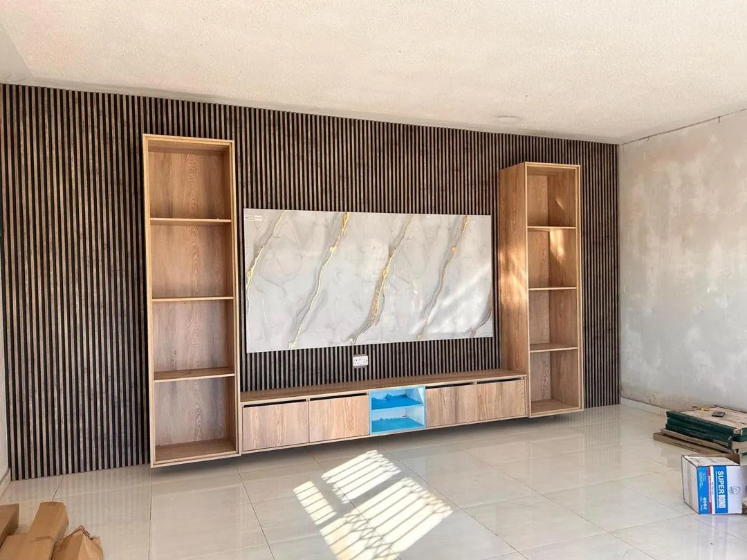 Living room wall with dark fluted panels, tall wooden shelves, a marble-look feature panel and a low media cabinet