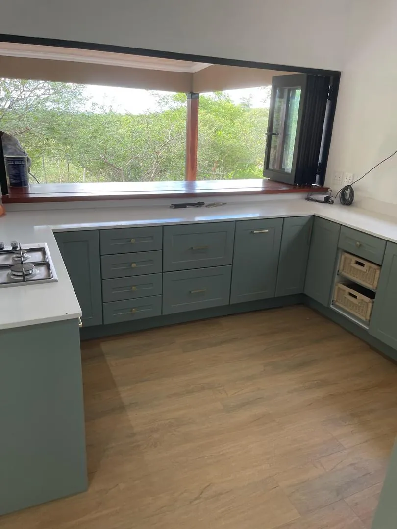 Kitchen with sage-green cabinets, a white worktop and a window counter looking onto trees