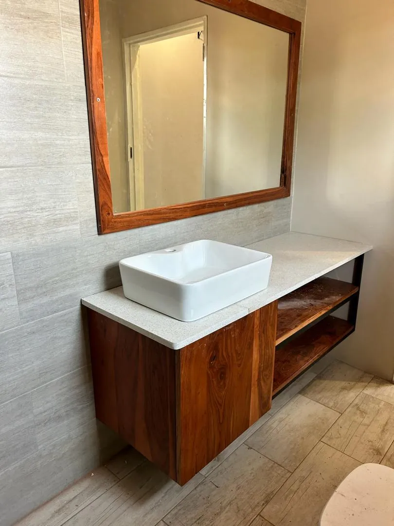 Floating wooden bathroom vanity with a white basin, a stone-look top and a wood-framed mirror